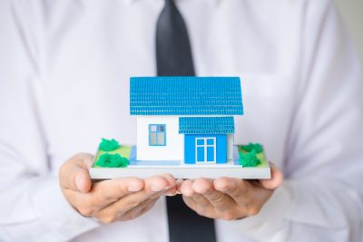 Businessman Holding Model House In Palm Of Hand